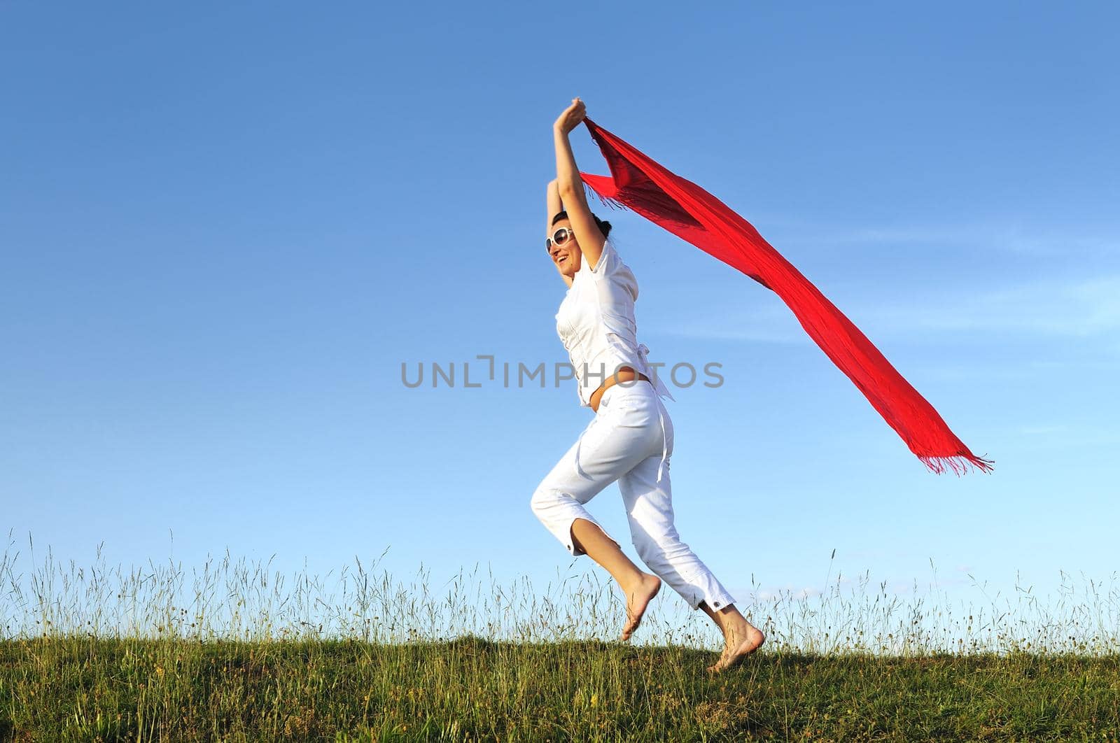 beautiful young and healthy woman run and jump on meadow at sunny day with red scarf