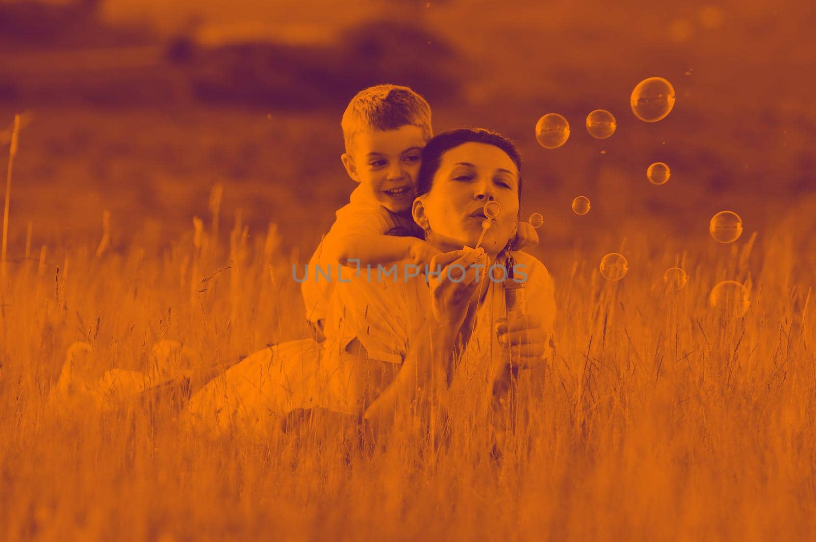 happy child and woman outdoor playing with soap bubble on meadow duo tone
