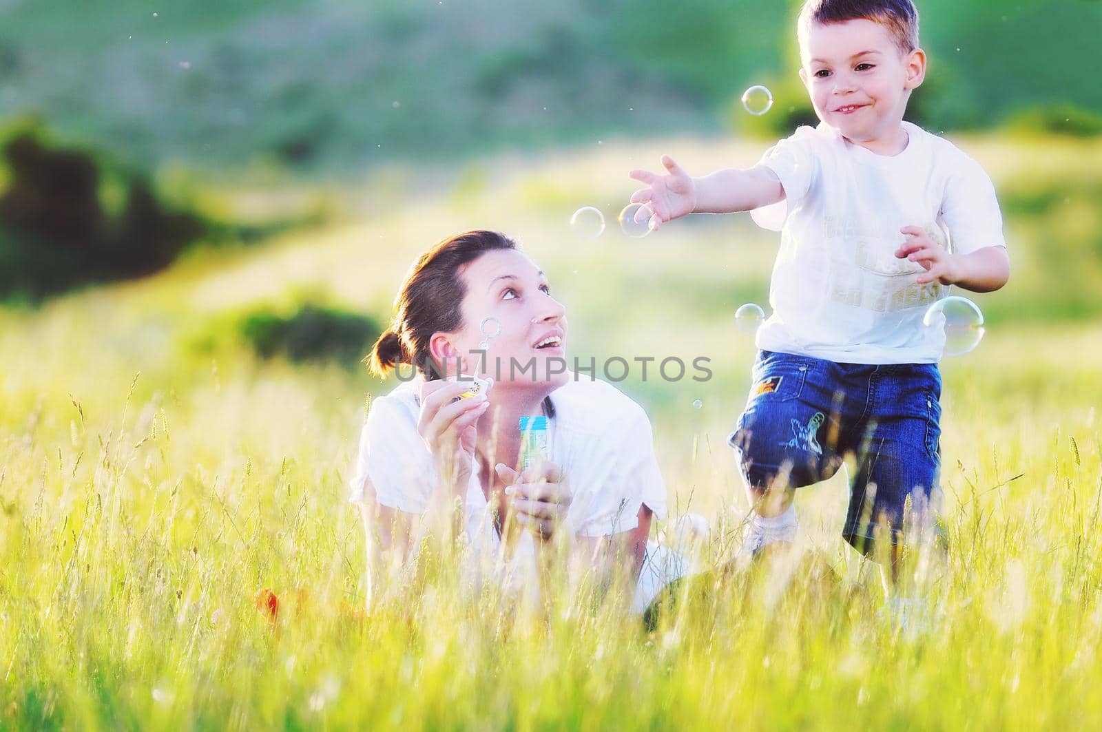 happy child and woman outdoor playing with soap bubble on meadow