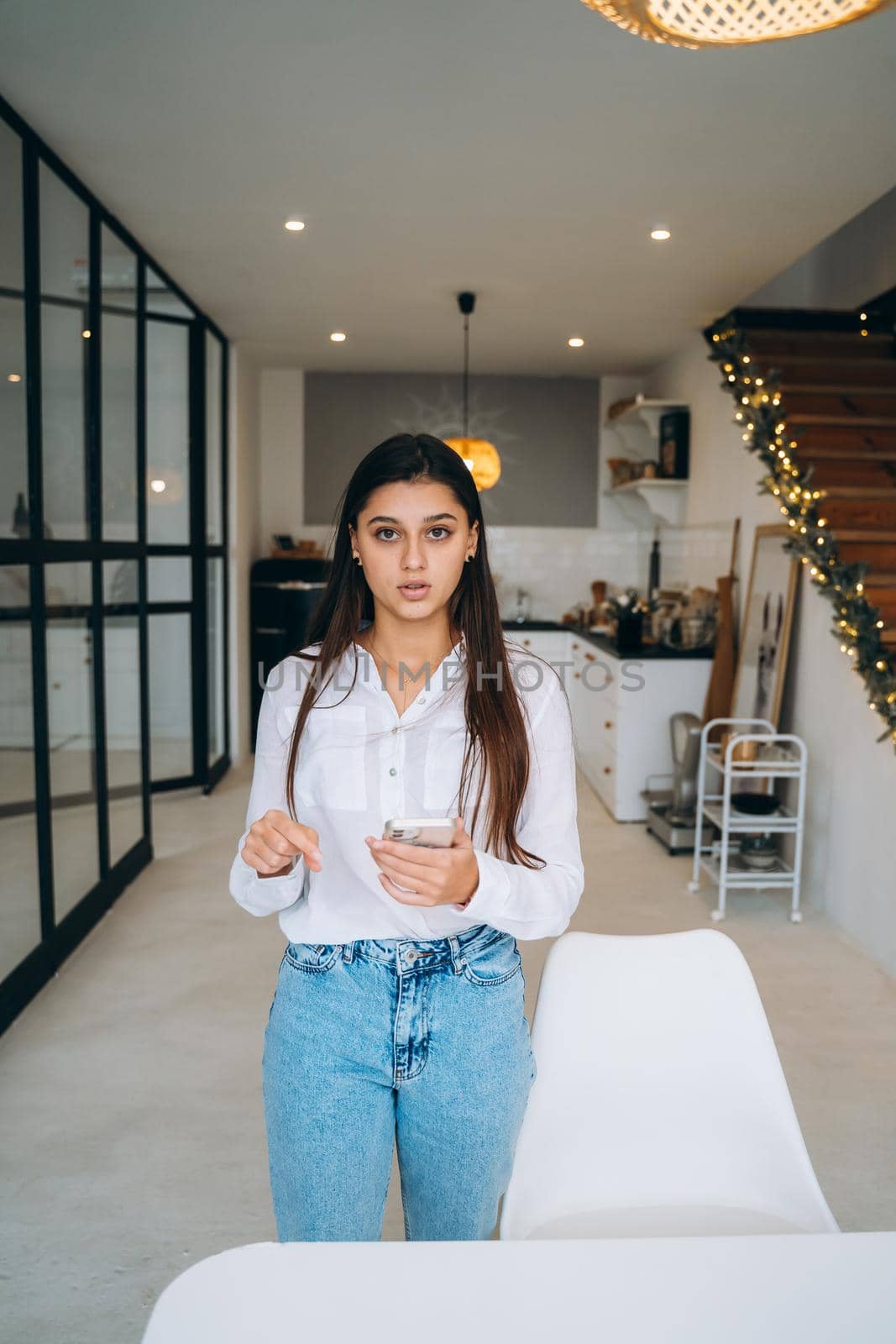 Young attractive Caucasian woman with long hair looking at camera on her phone, holding modern gadget in hands