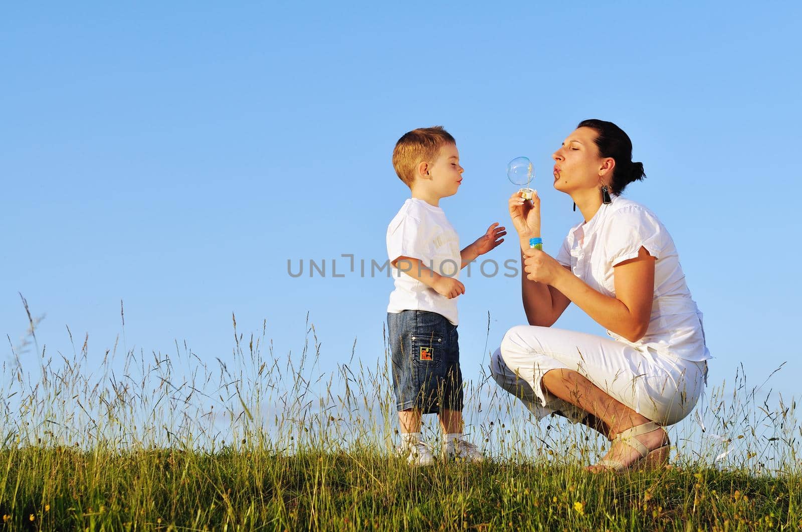 happy child and woman outdoor playing with soap bubble on meadow