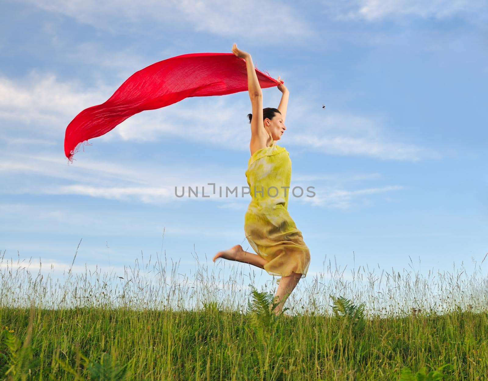 beautiful young and healthy woman run and jump on meadow at sunny day with red scarf