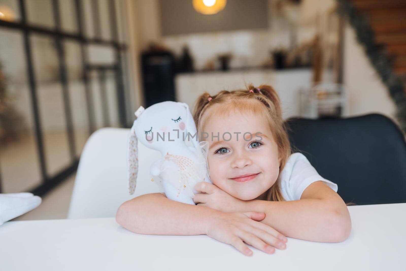 Little smiling girl hugging favorite toys while sitting at table happy childhood