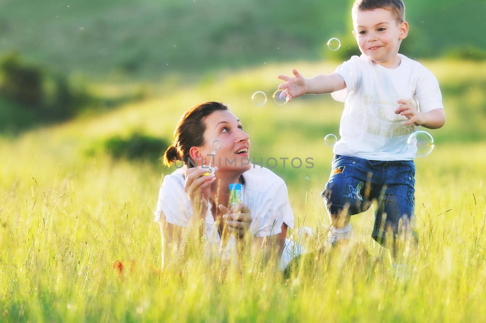 happy child and woman outdoor playing with soap bubble on meadow