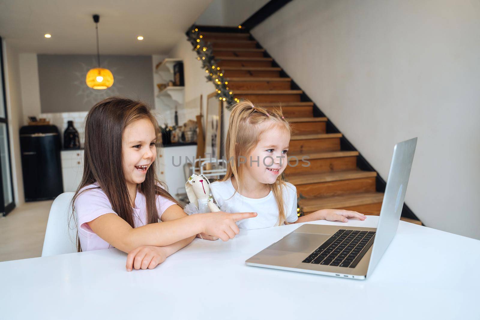 Two little girls playing together at the laptop while sitting