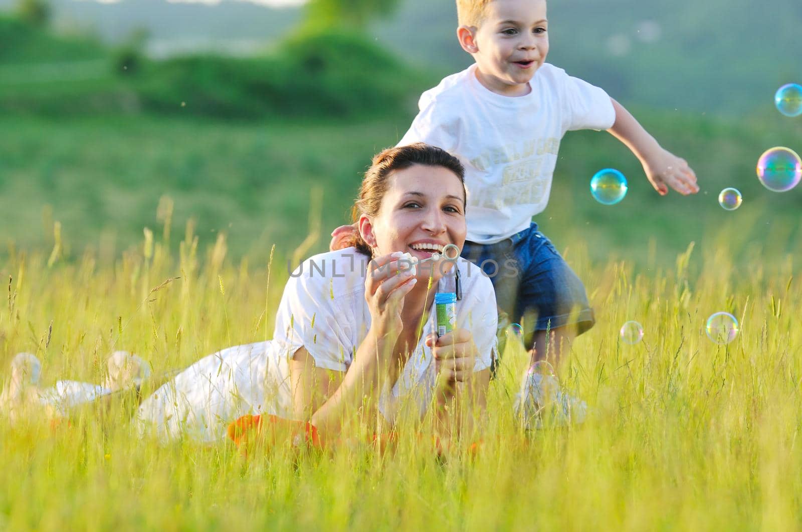 happy child and woman outdoor playing with soap bubble on meadow