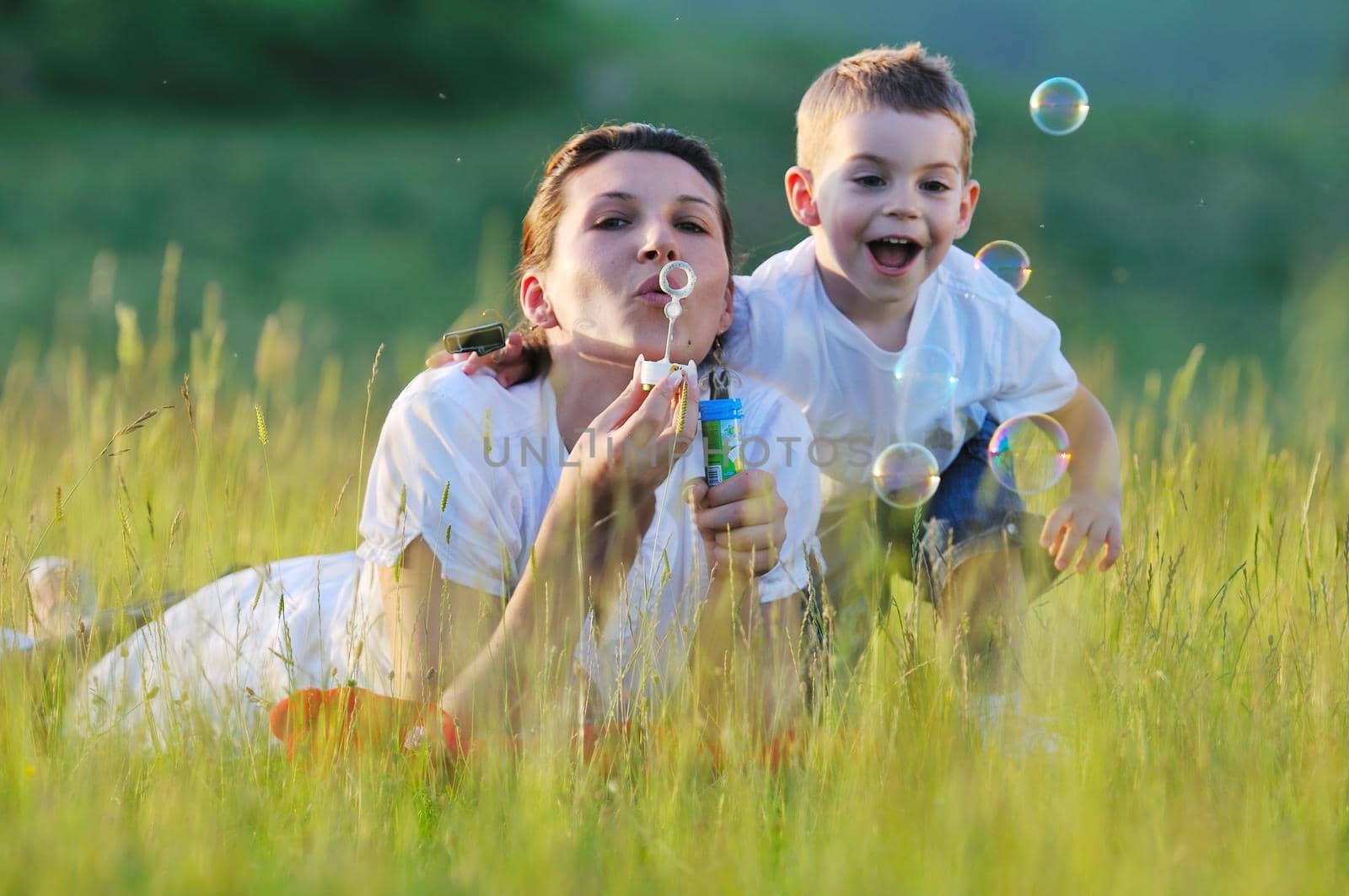 happy child and woman outdoor playing with soap bubble on meadow