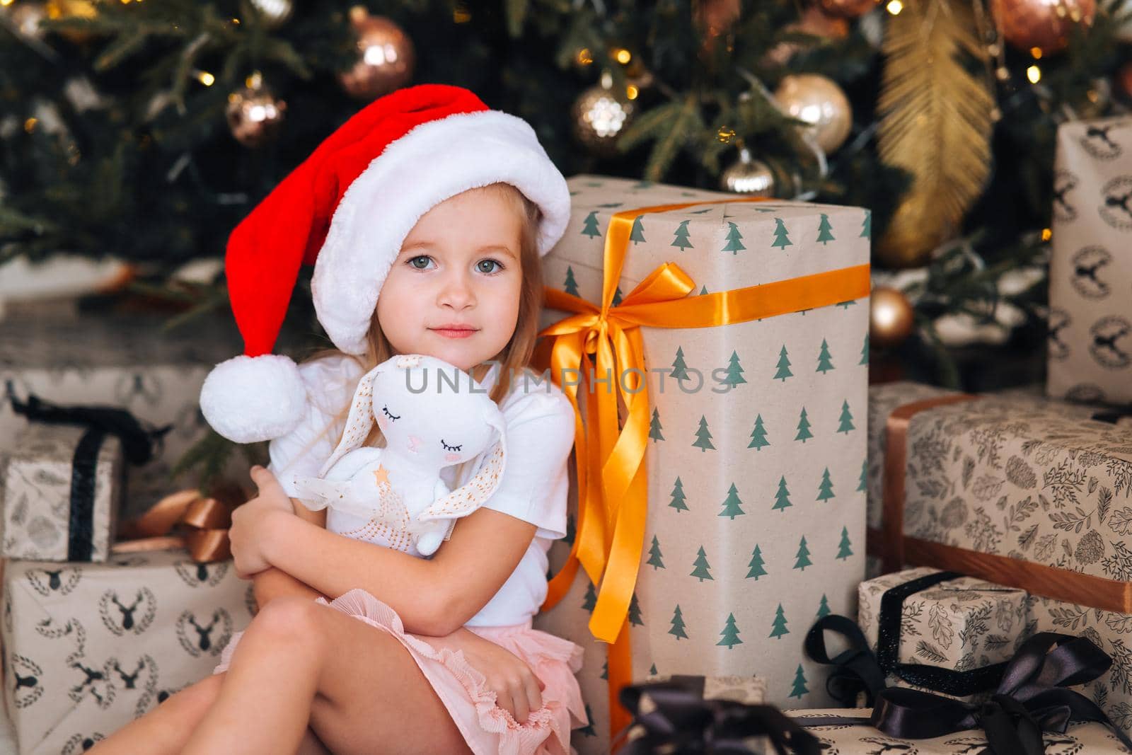 Happy little girl hugs her favorite toy in the room decorated for the New Year and Christmas