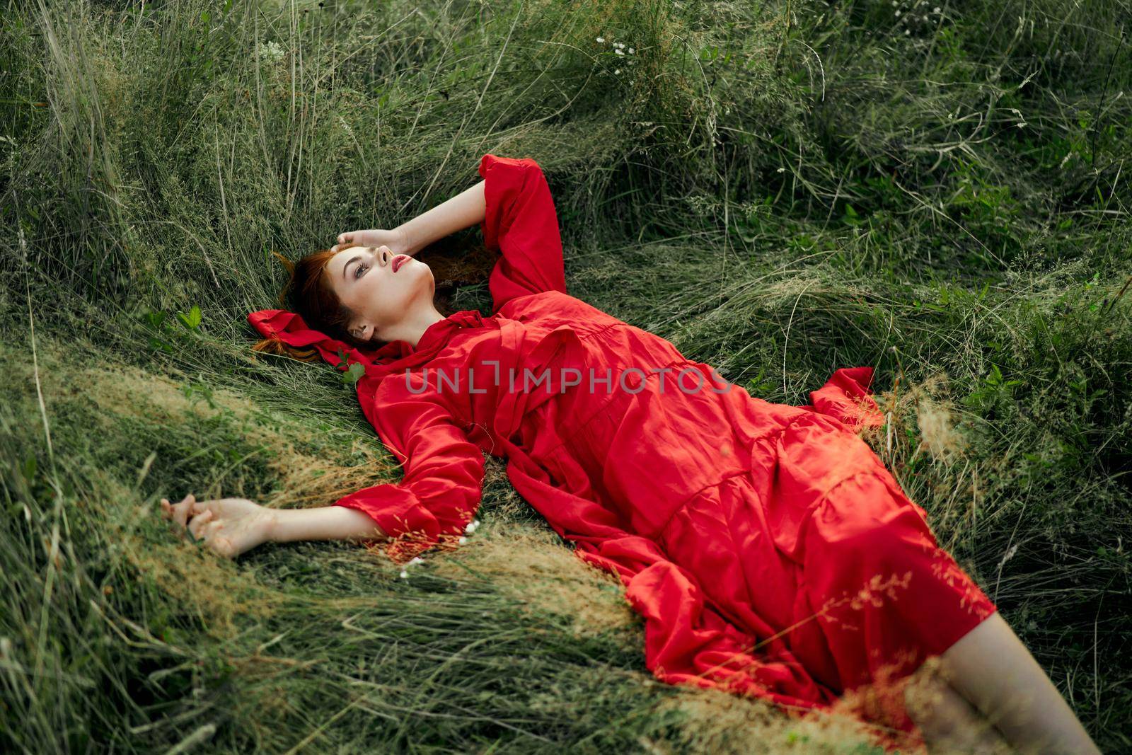 woman in red dress lies on the grass in the field nature landscape. High quality photo