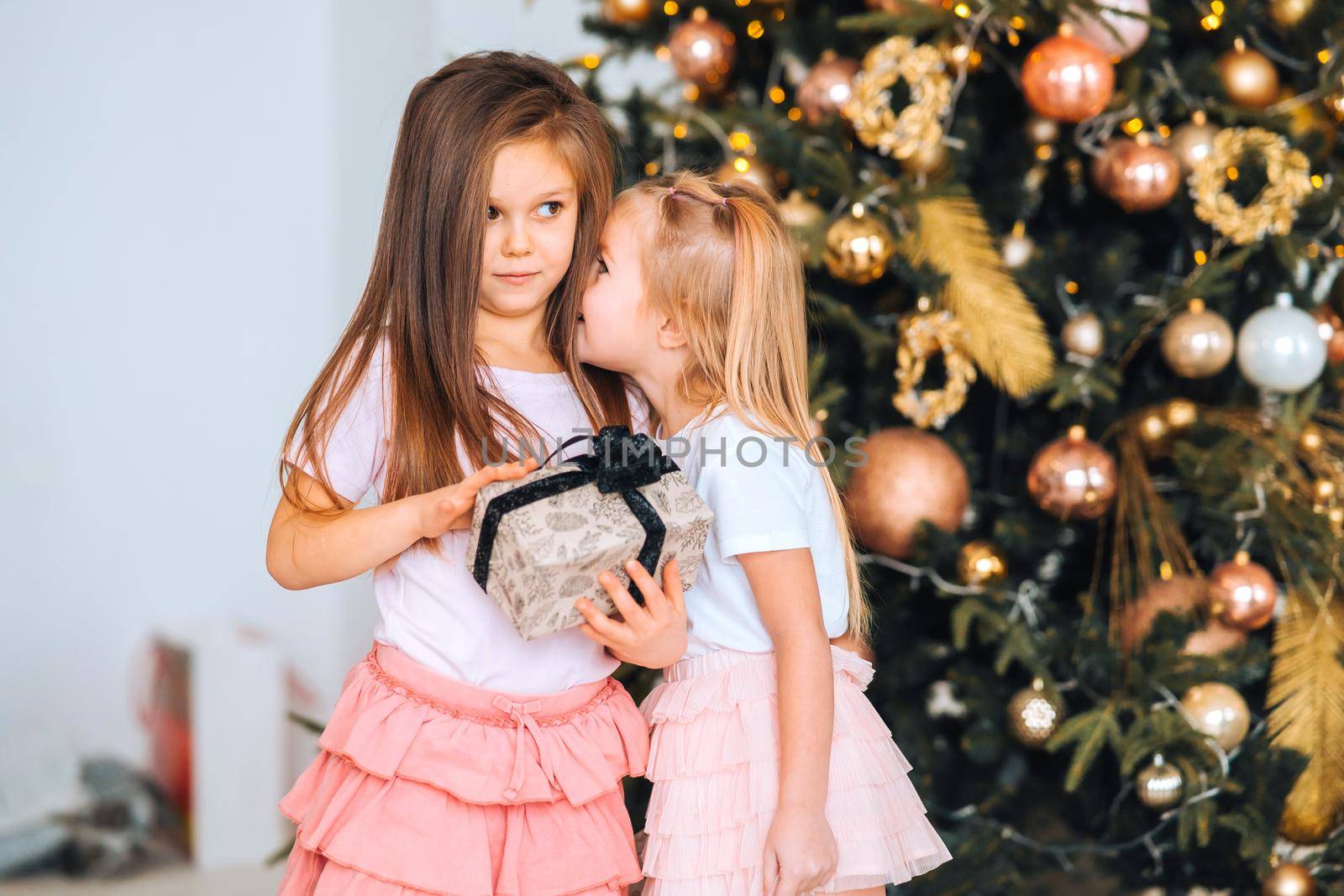 Charming little girls holds a gift on a background of Christmas trees by teksomolika