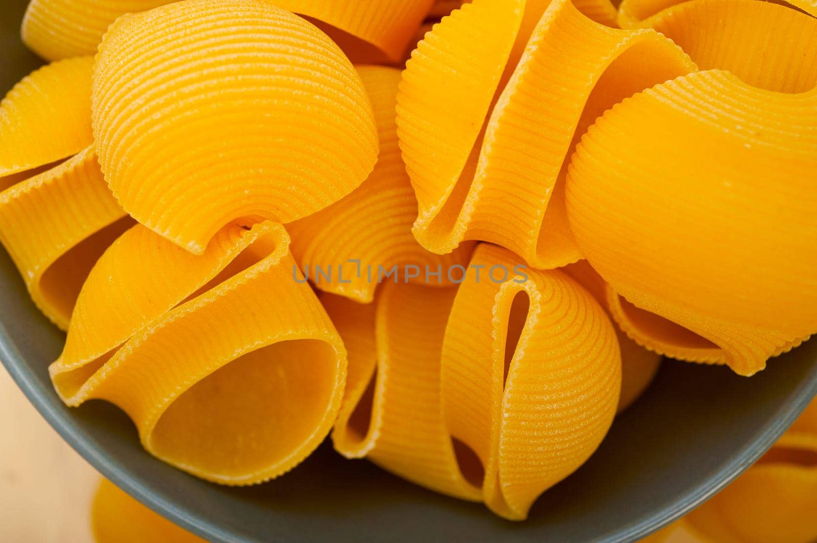 raw Italian snail lumaconi pasta on a blue bowl over rustic table macro