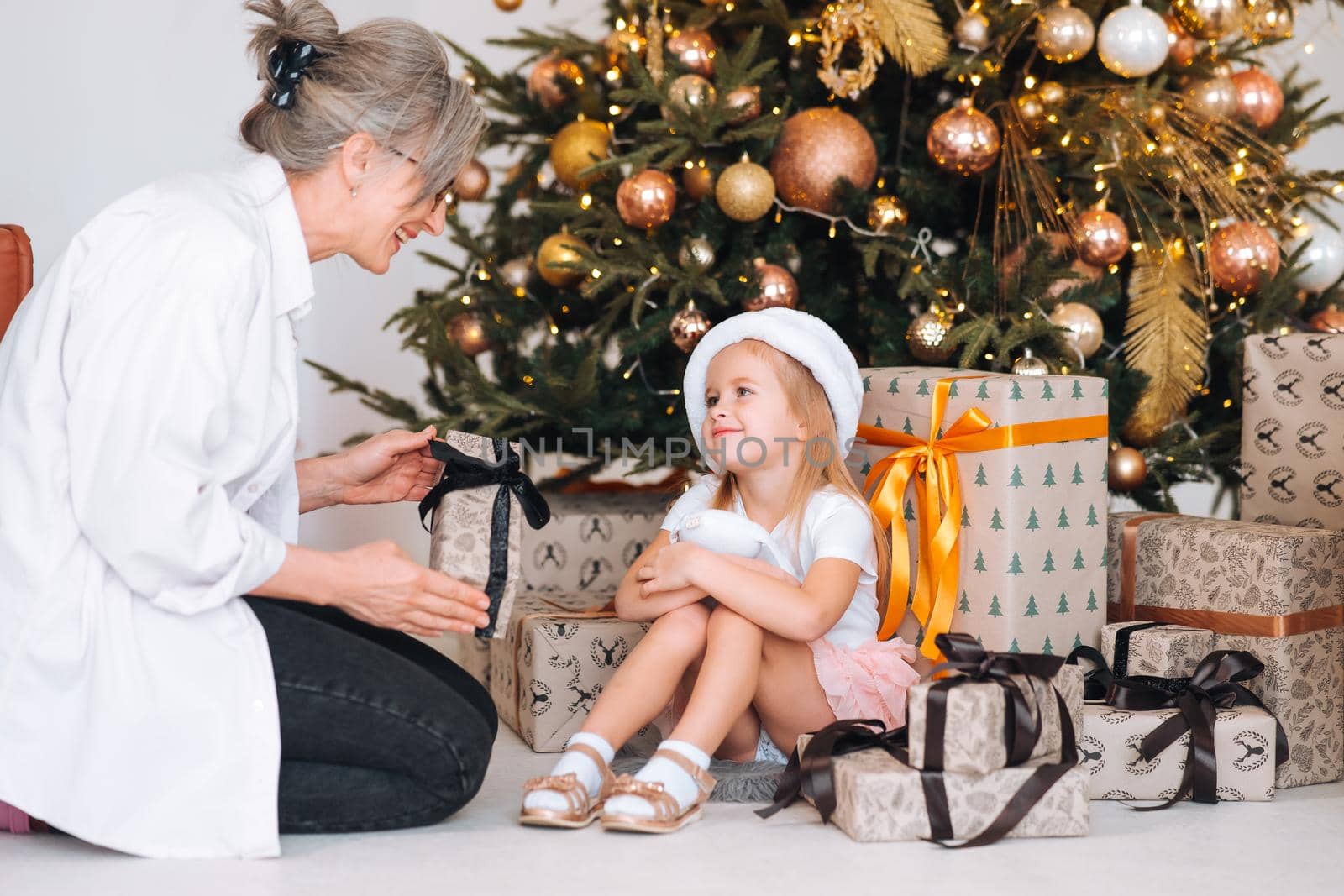 Happy grandmother giving christmas present to excited granddaughter. Lovely grandma and child exchange gifts