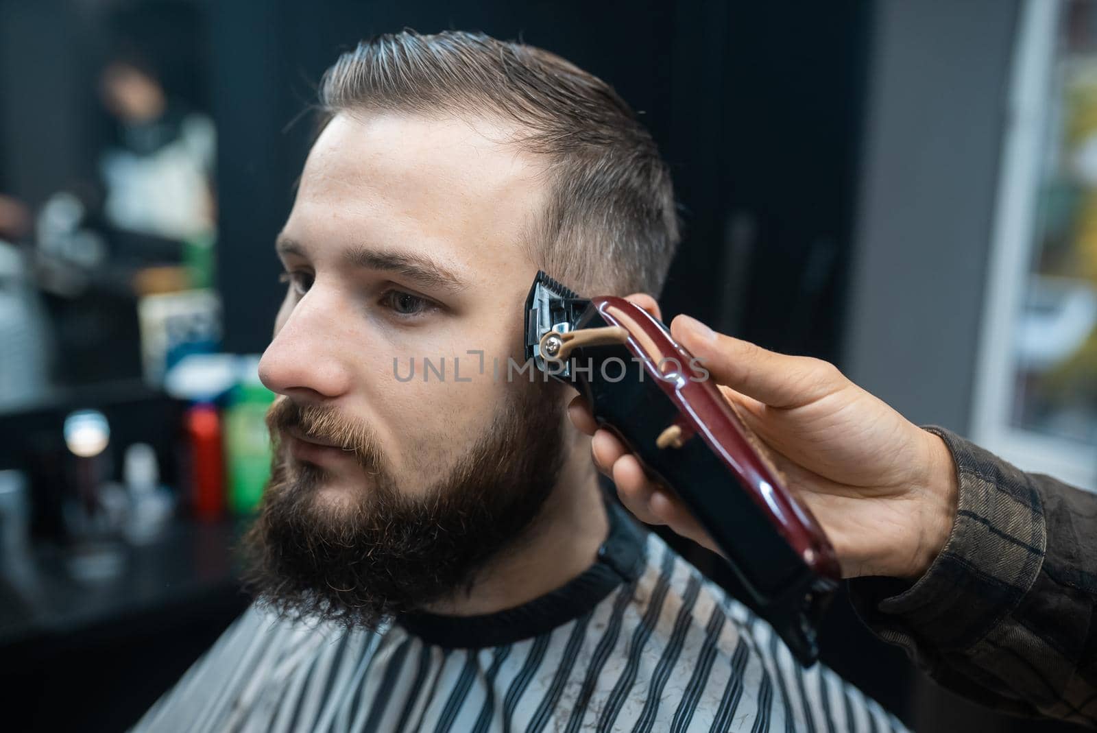 Master in barbershop makes men's haircutting with hair clipper by teksomolika
