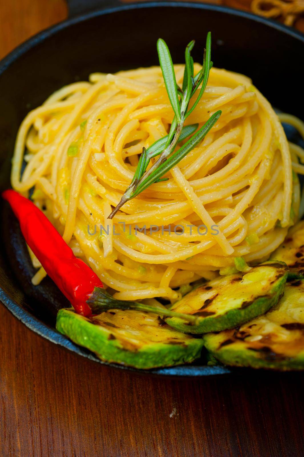 italian spaghetti pasta with zucchini sauce on iron skillet over wood board