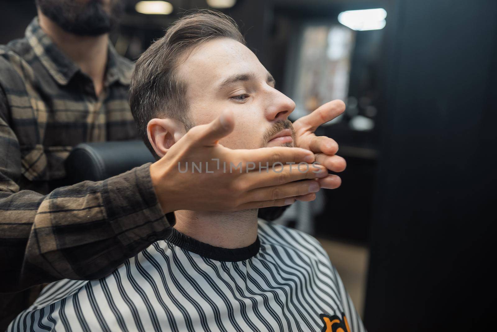 Facial applying lotion after shave in Barber shop. Master hands close up