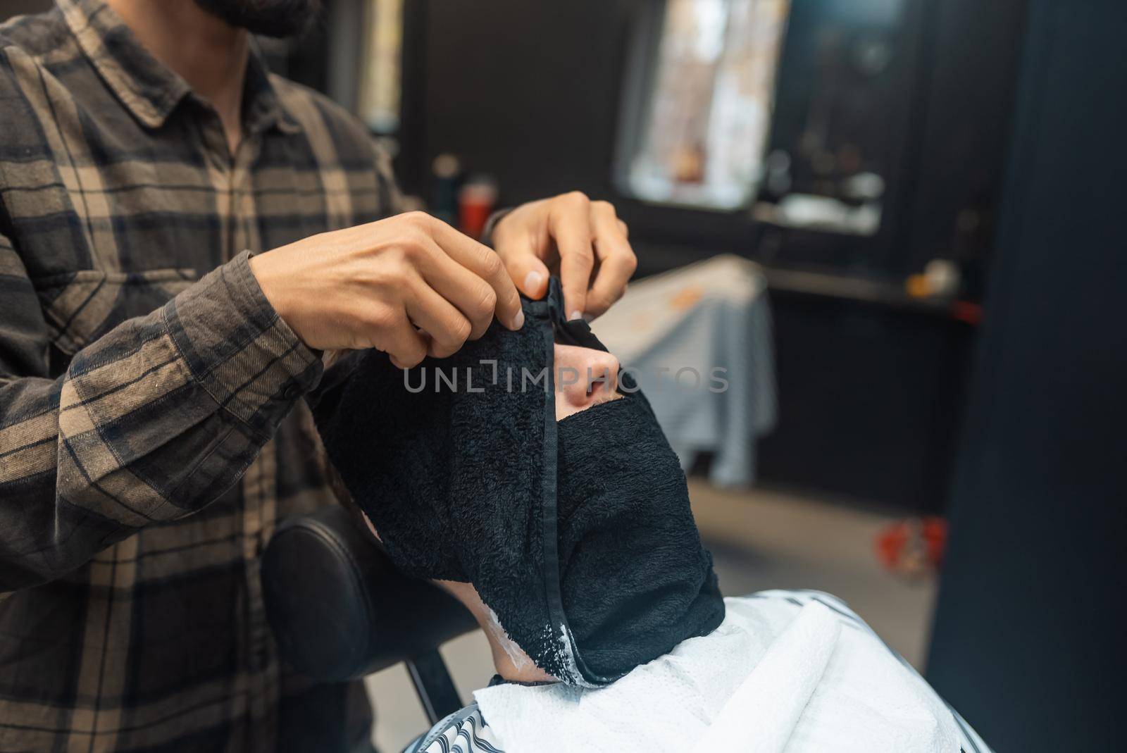 Barber preparing man face for shaving with hot towel in barber shop by teksomolika