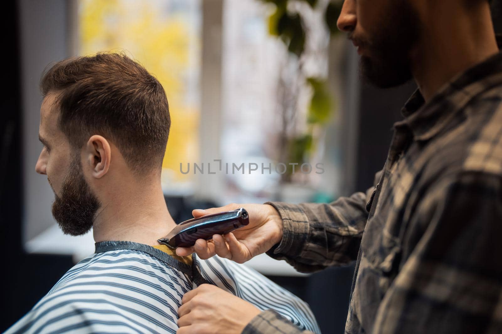 Master in barbershop makes men's haircutting with hair clipper by teksomolika