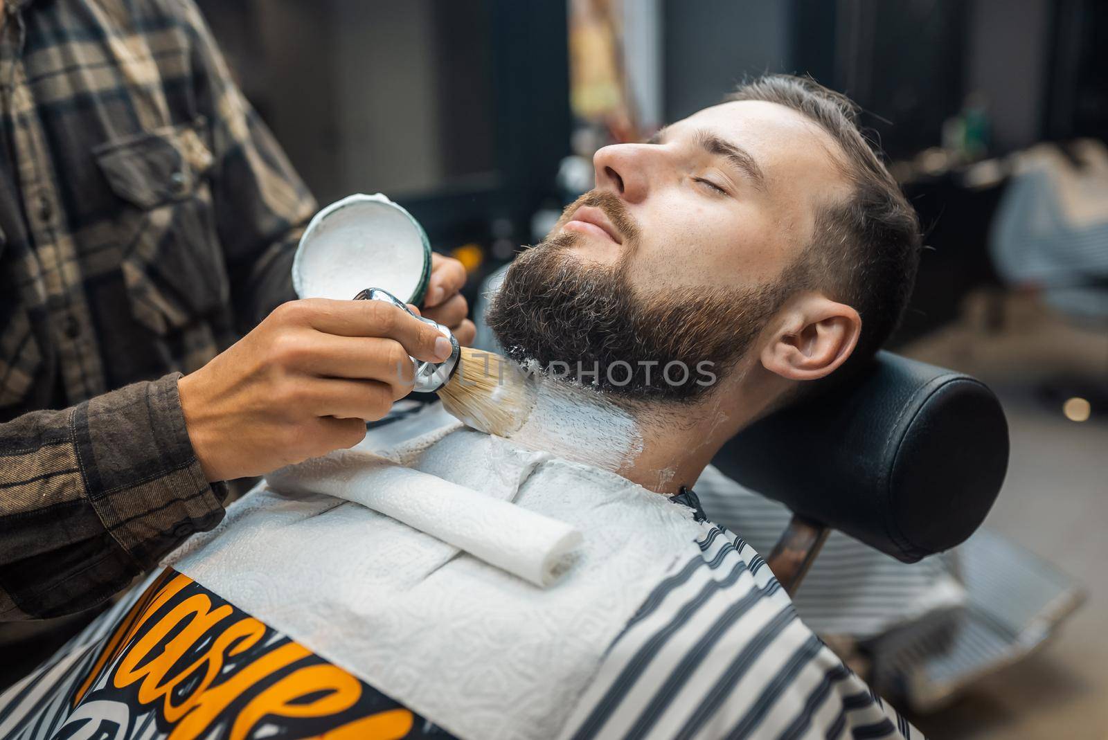 Master applying shaving foam on client face by teksomolika