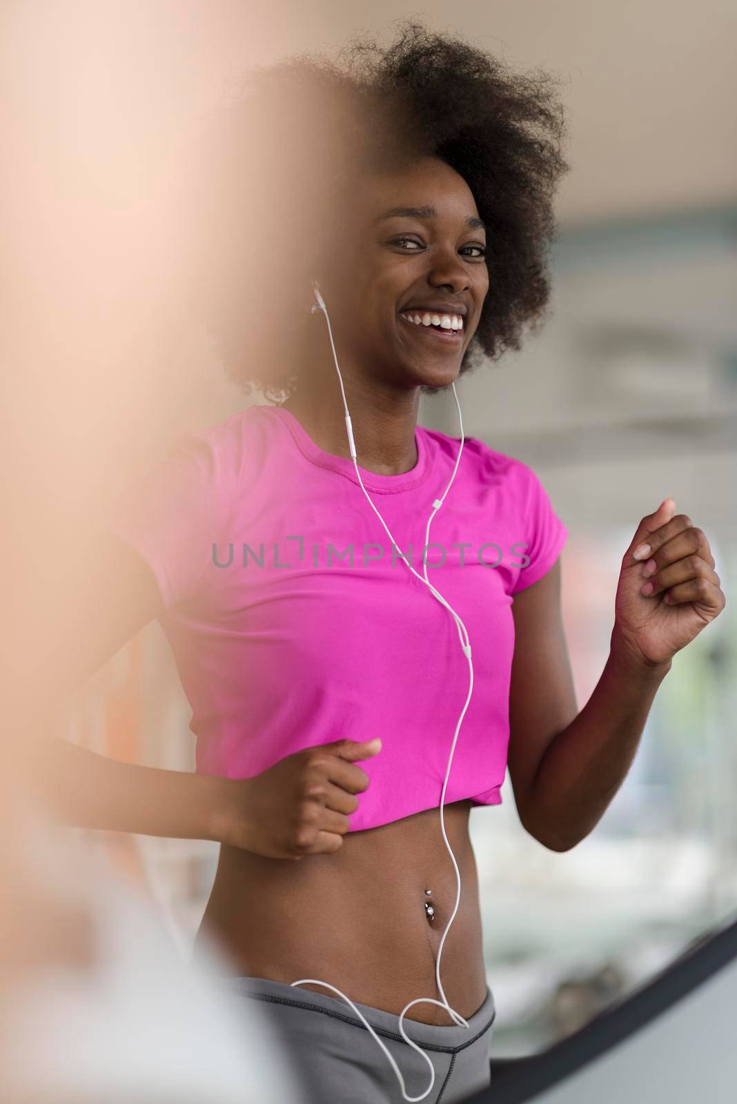 afro american woman running on a treadmill at the gym while listening music on earphones