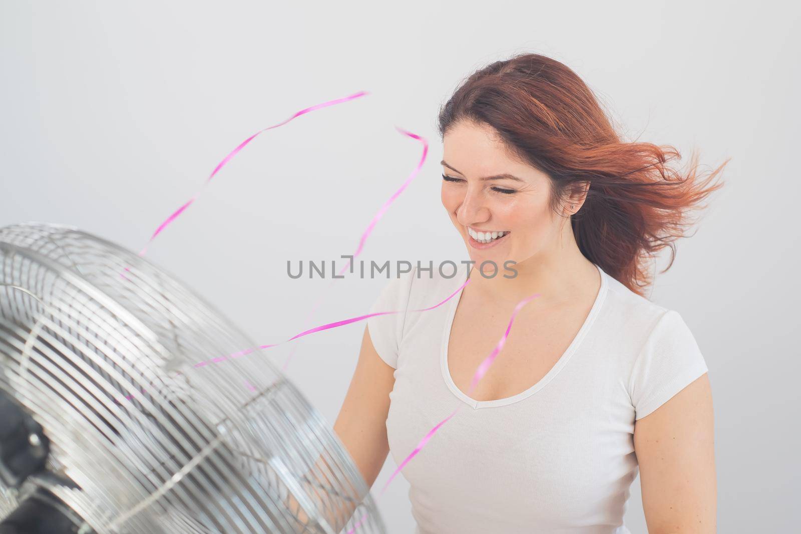 Joyful caucasian woman enjoying the wind blowing from an electric fan on a white background. by mrwed54
