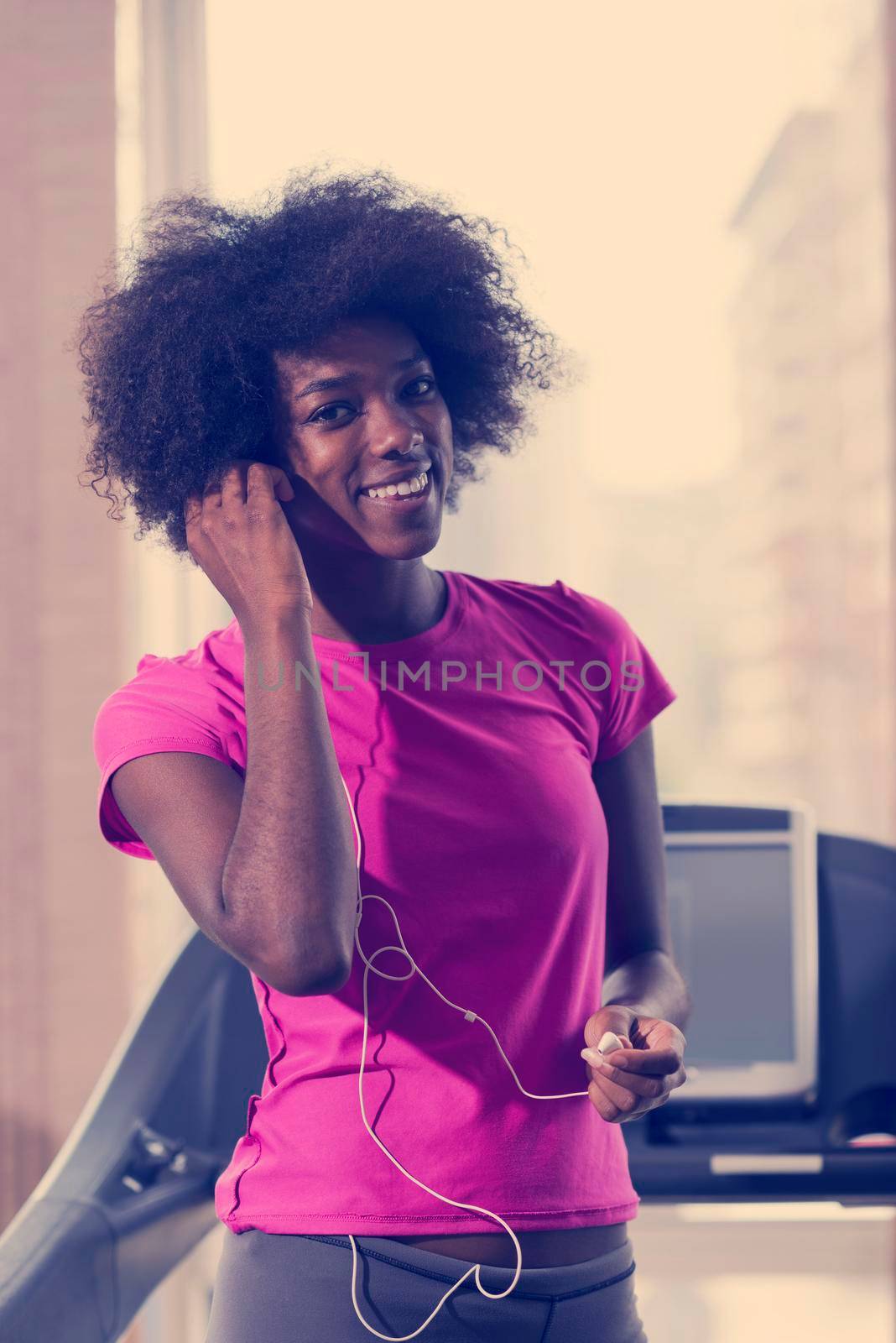 afro american woman running on a treadmill at the gym while listening music on earphones