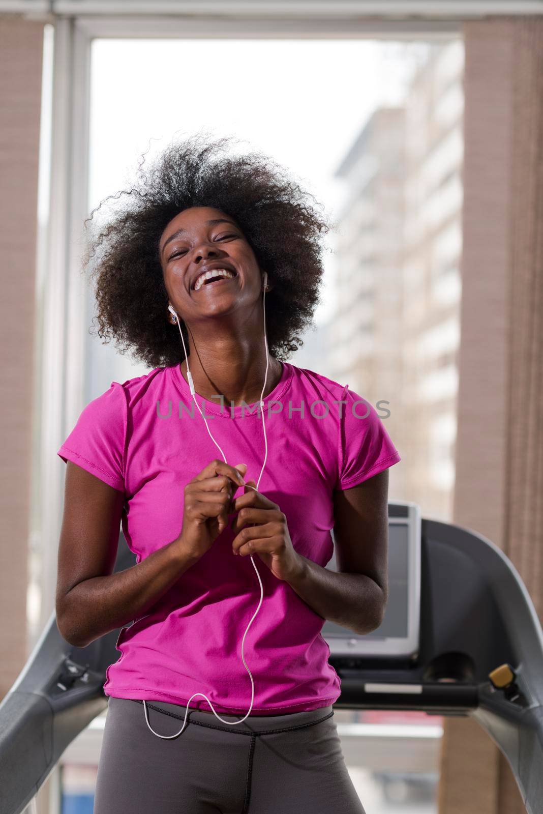 afro american woman running on a treadmill at the gym while listening music on earphones