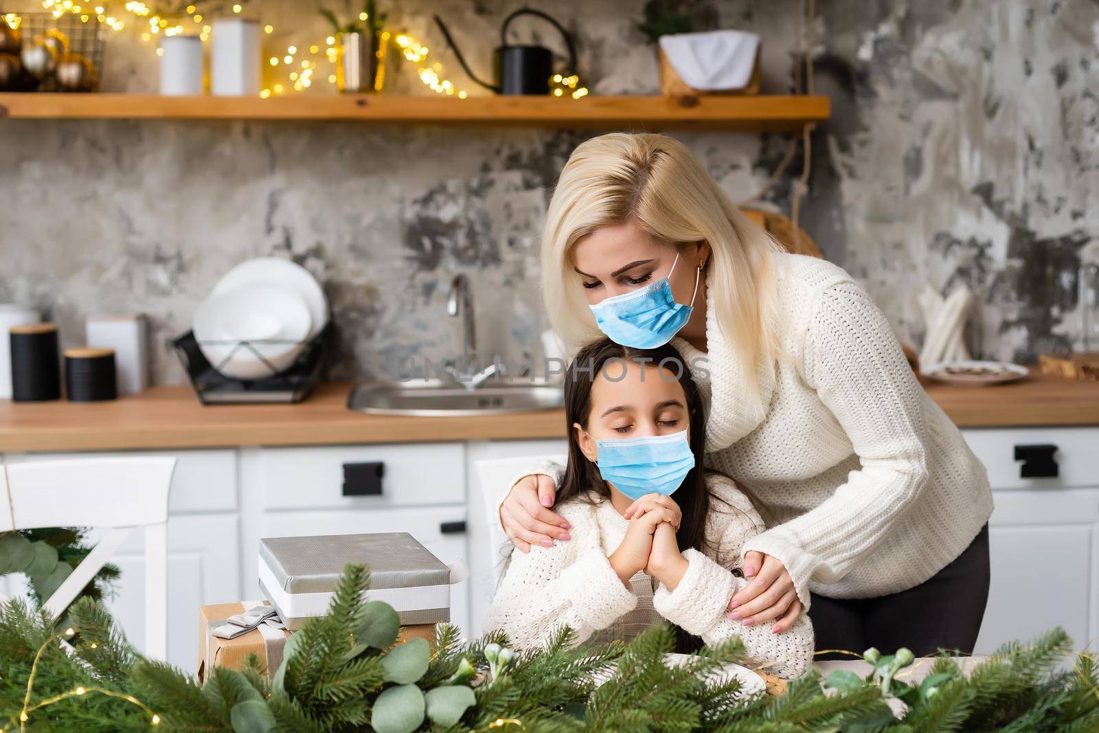Beautiful mother and daughter in medical masks have fun at home near the Christmas tree in a interior. Family happiness, holiday, joy, vacation, games with a woman. New Year's preparations.