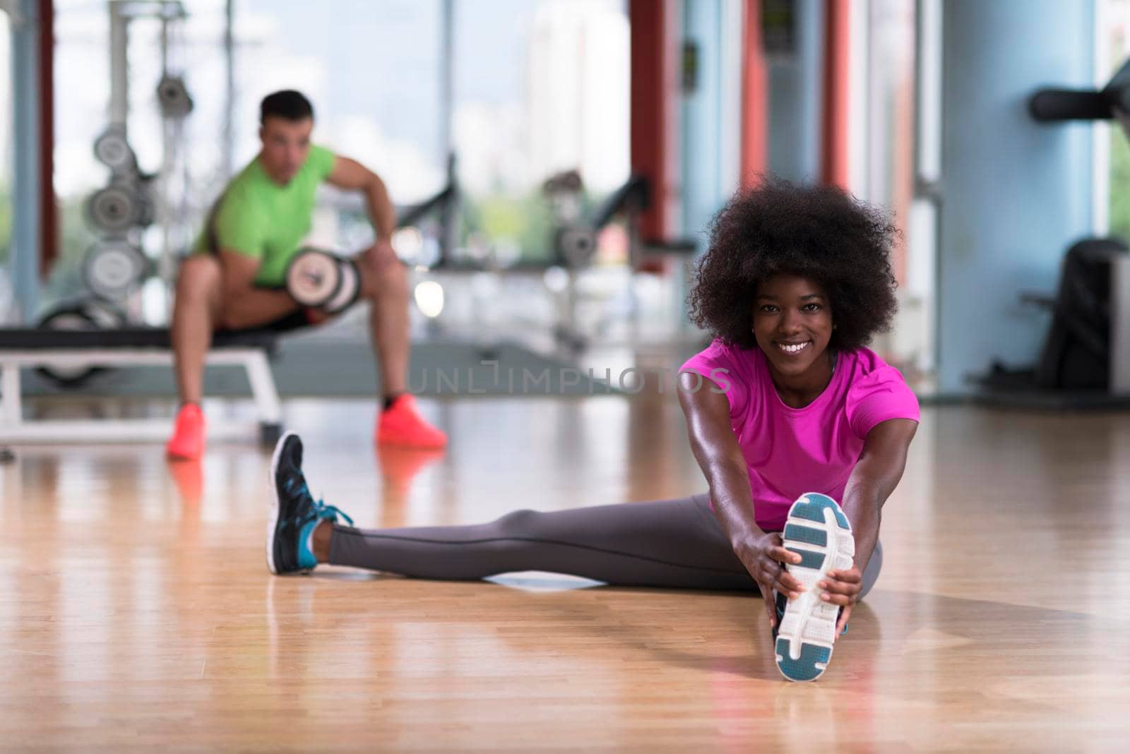 woman in a gym stretching and warming up man in background working with dumbbels by dotshock