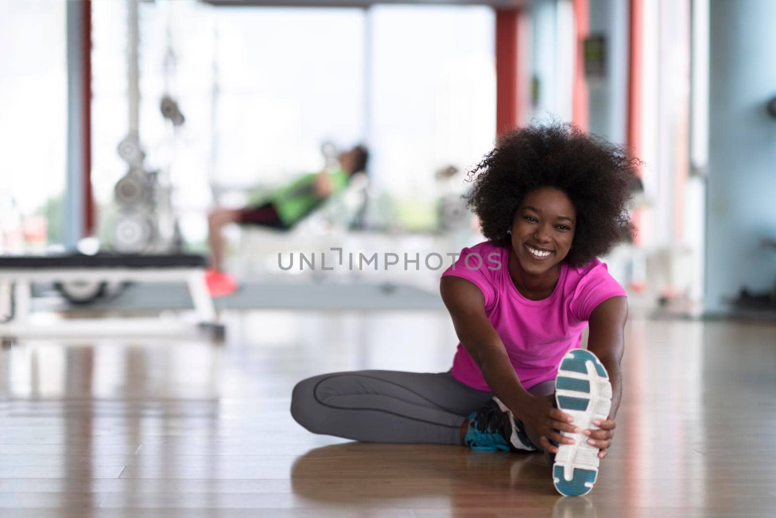 woman in a gym stretching and warming up man in background working with dumbbels by dotshock