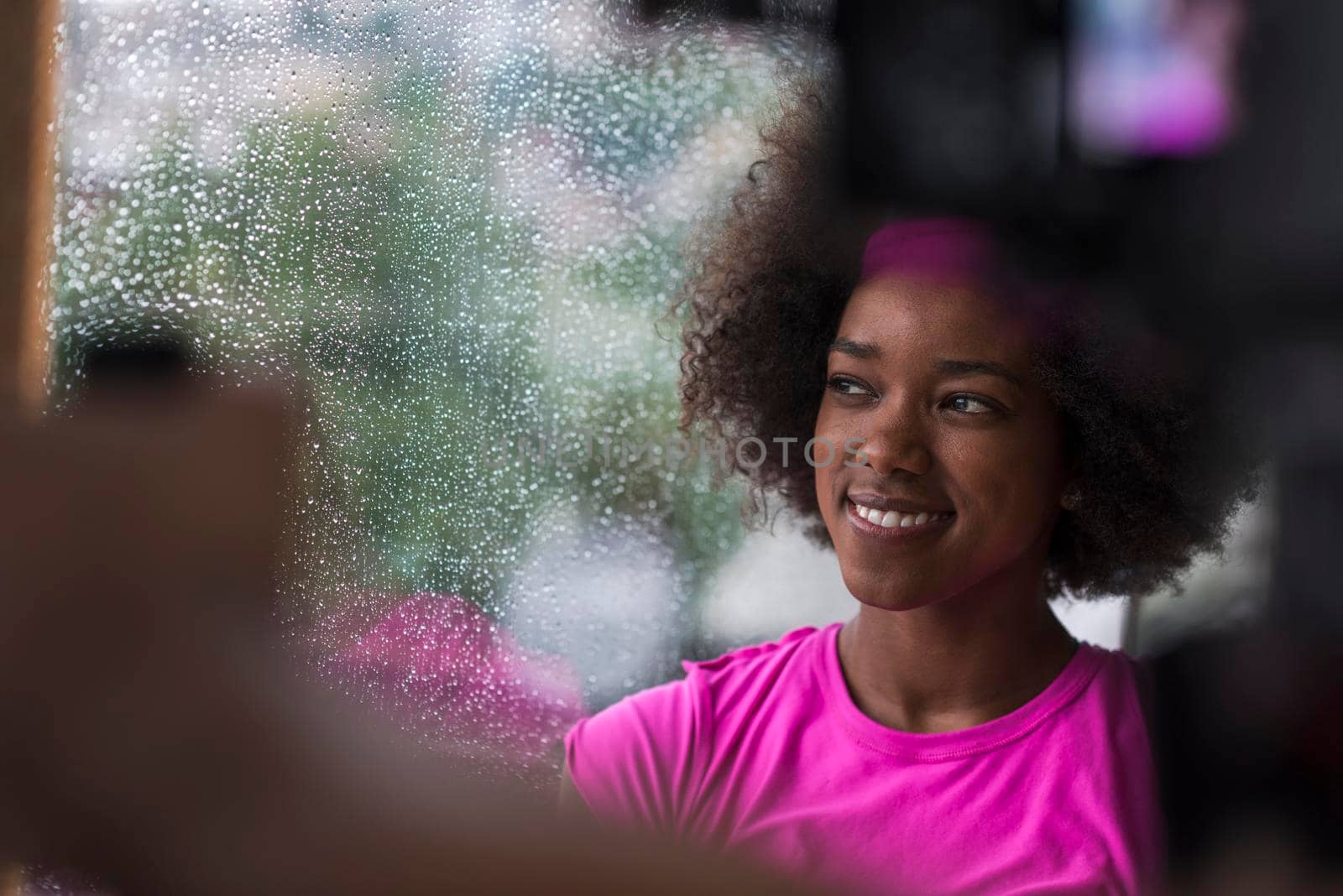 beautiful african american woman using tablet computer from home while rain and bad weather is outdoor