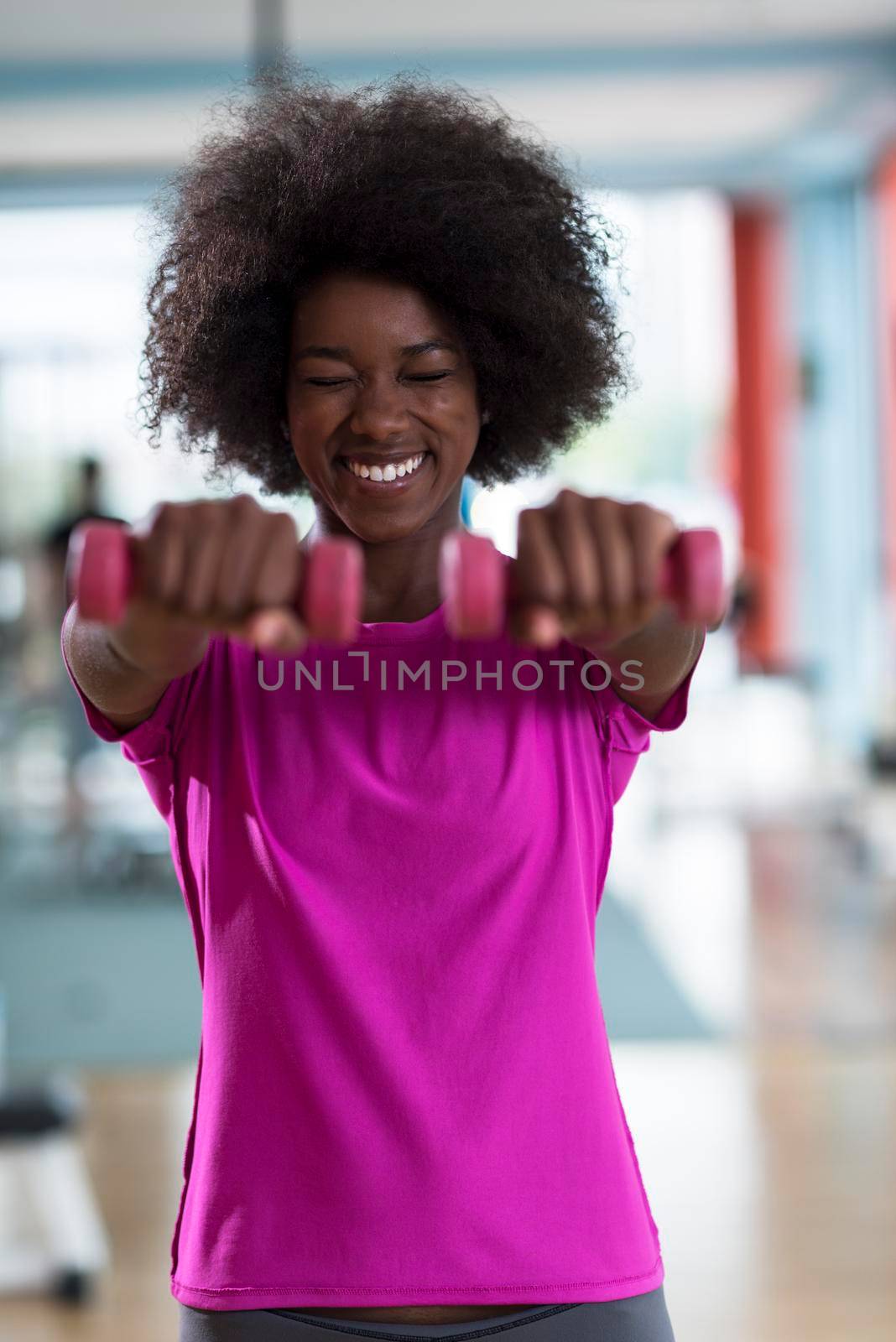 happy healthy african american woman working out in a crossfit gym on weight loss with dumbbells