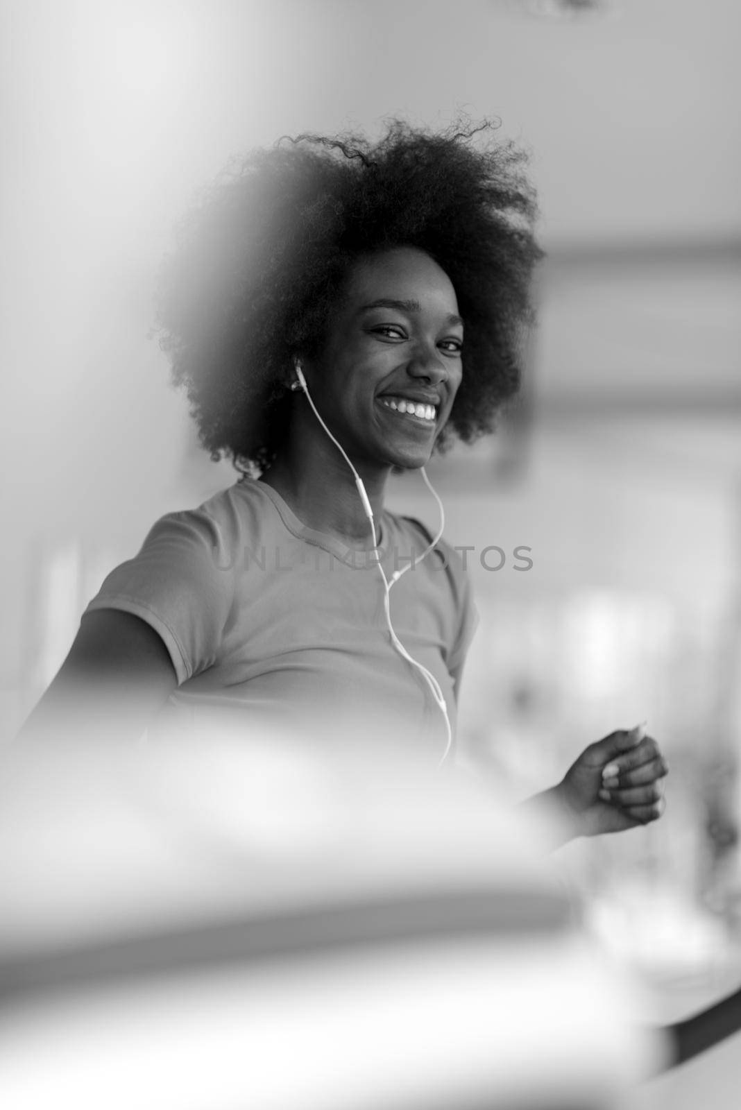 afro american woman running on a treadmill at the gym while listening music on earphones