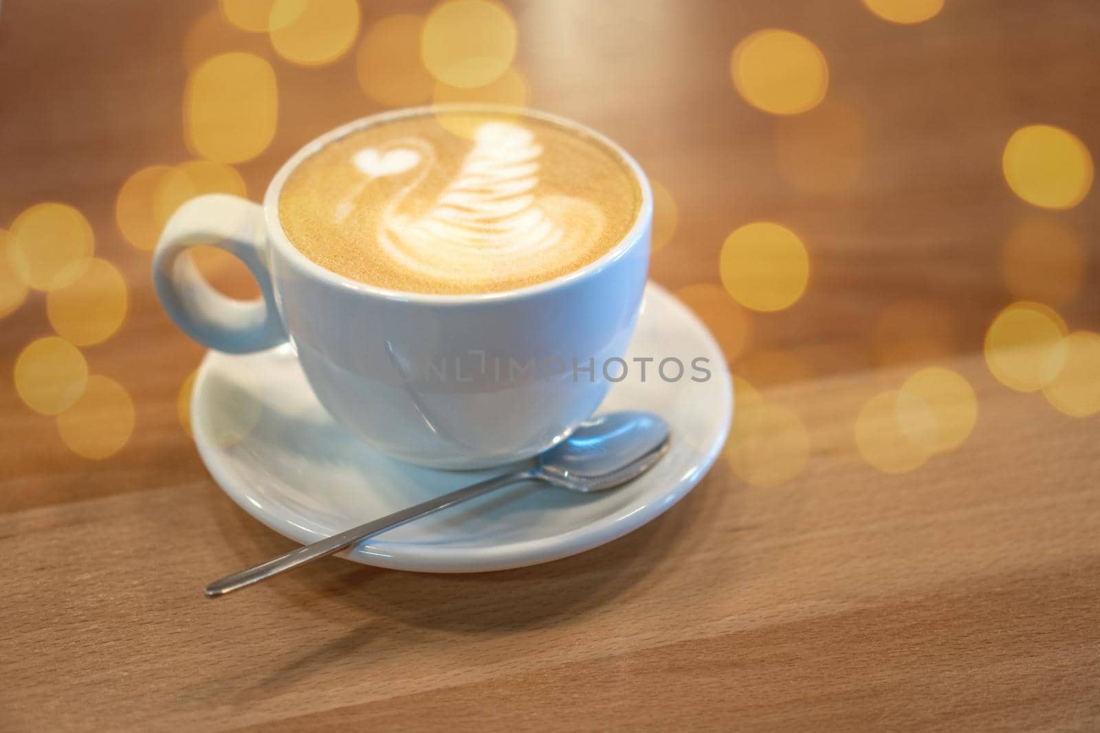 White cup of coffee with latte art standing on wooden table in a cafe. Cappuccino with milk decoration. Morning breakfast. Cozy meal with hot beverage concept