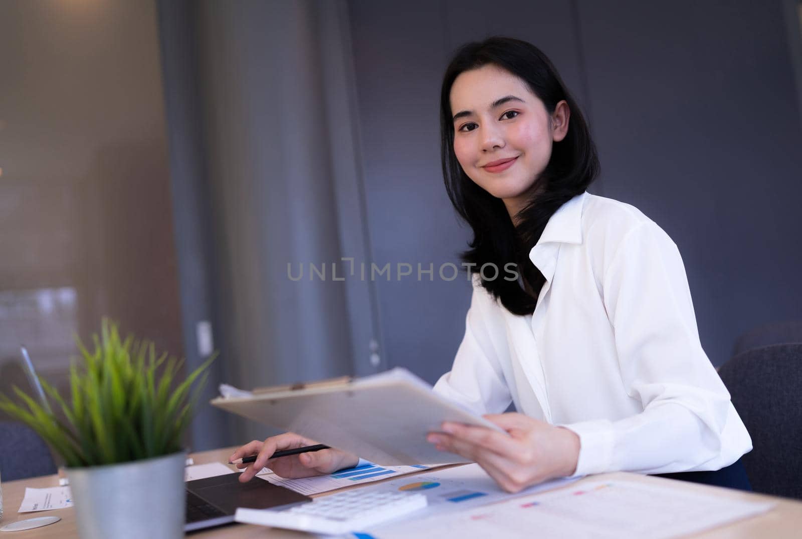 Portrait. Asian Office girl looking at camera and smiling working on company information, Laptop computers, office equipment at the workplace. Banner and copy space.