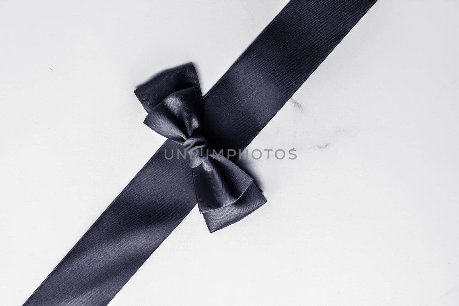 Holiday gift, decoration and sale promotion concept - Black silk ribbon and bow on marble background, flatlay