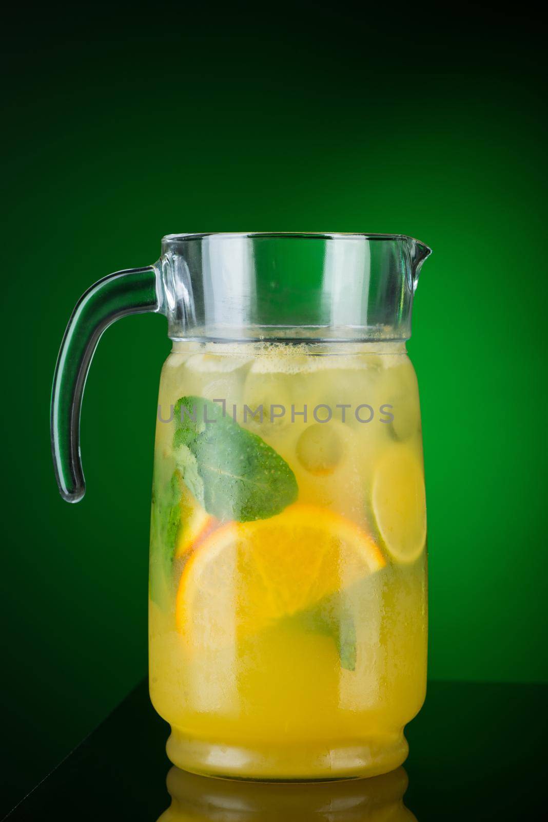 Cold drink of citrus in a decanter on a green background. Summer tropical juice