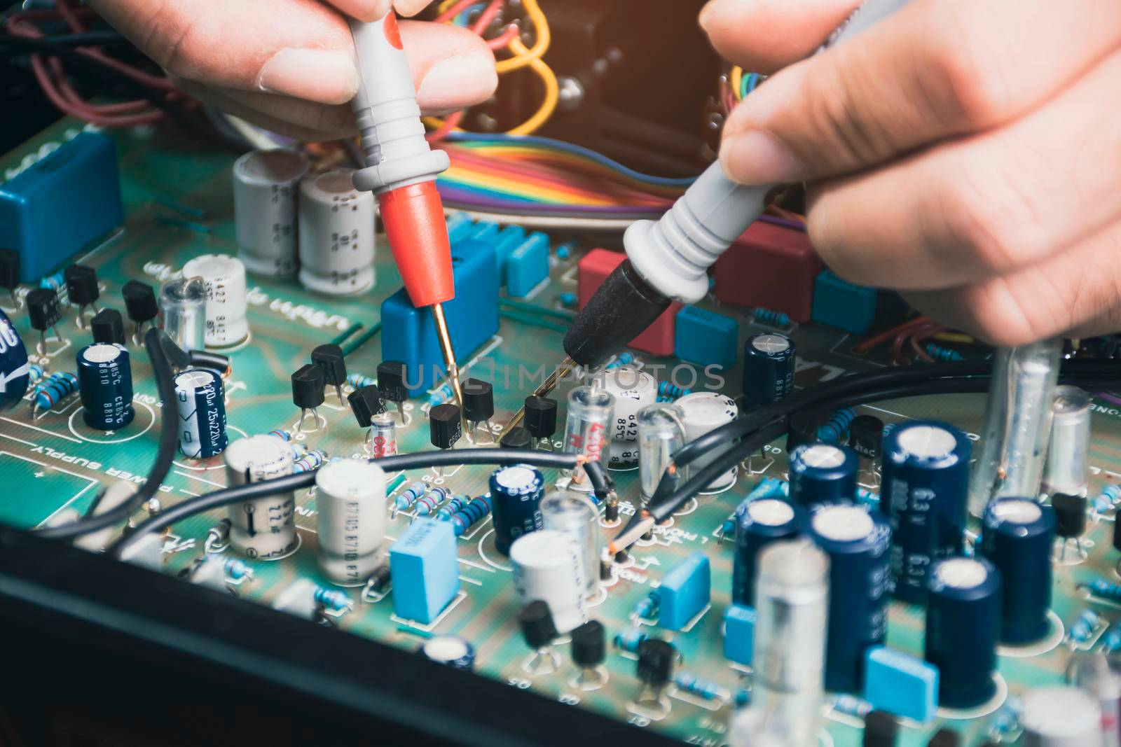 Electrician checking voltage of transistor in electronic circuit board with digital multimeter probe