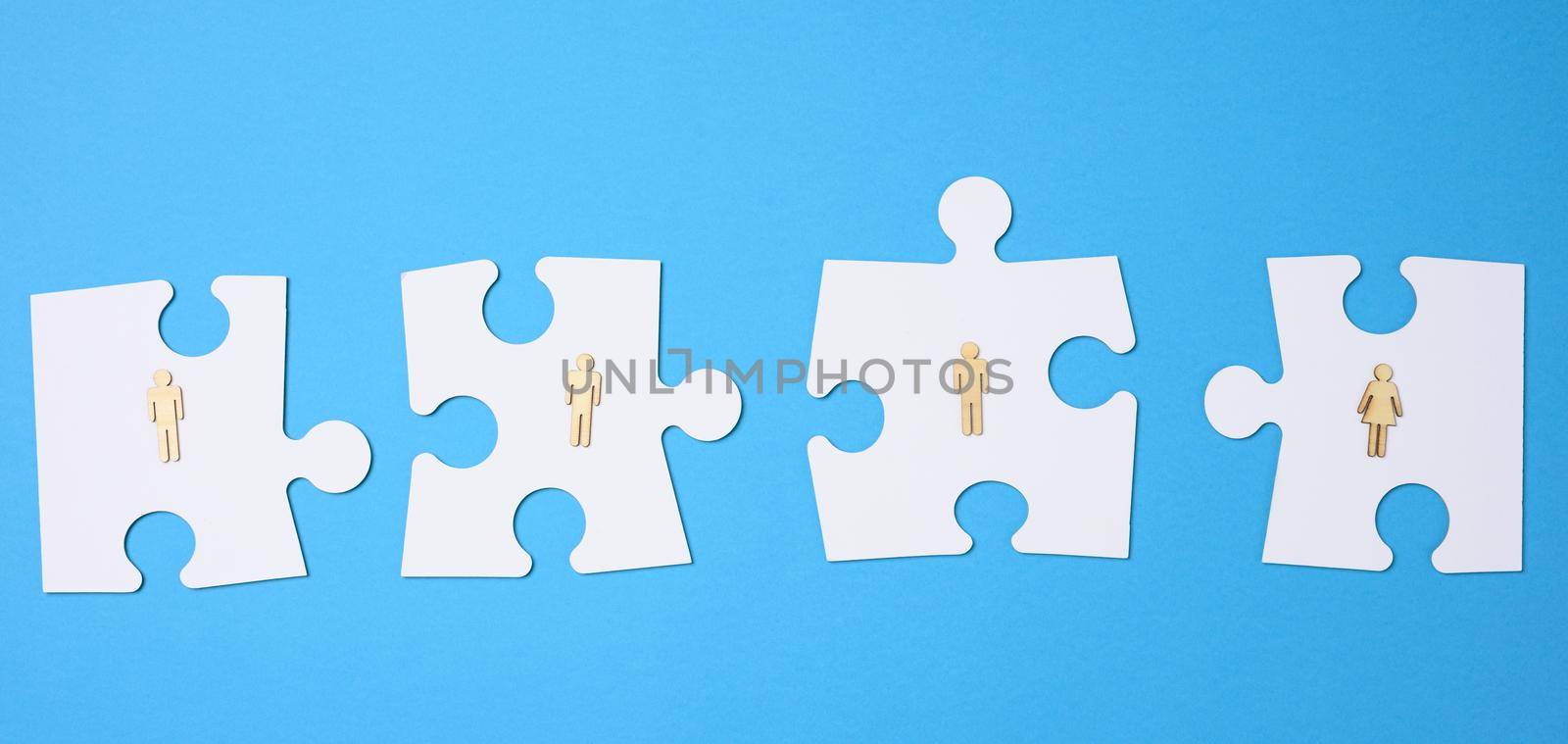 white puzzles and wooden men on a blue background. Personnel selection concept, team compatibility, individuality of each employee. Teamwork