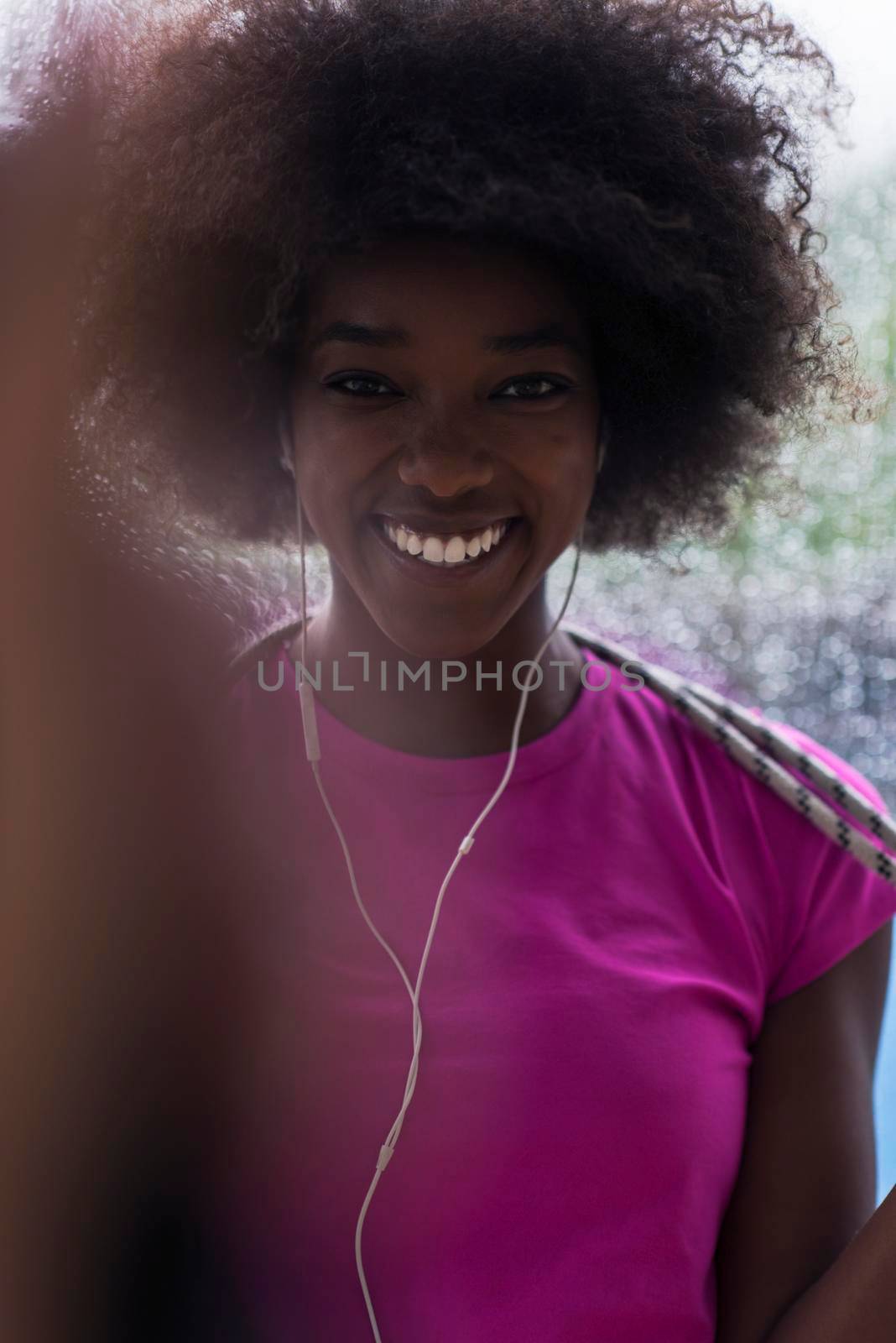 portrait of young afro american woman in gym on workout break while listening music on earphone  and dancing  rainy day and bad weather outdooor