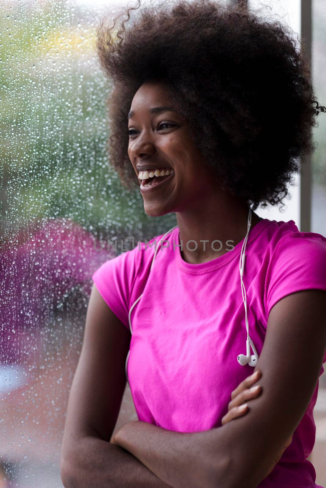 portrait of young afro american woman in gym on workout break while listening music on earphone  and dancing  rainy day and bad weather outdooor