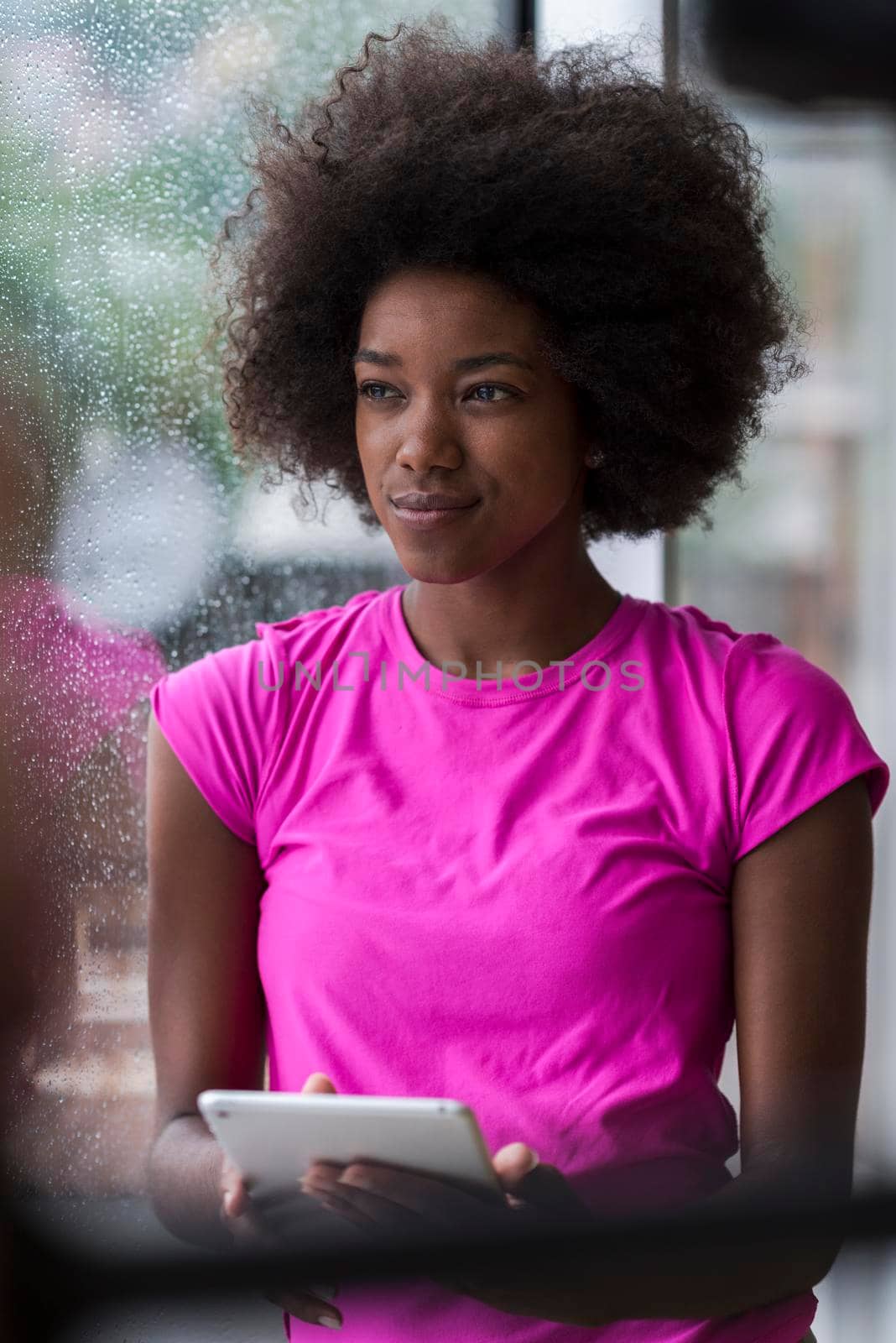 beautiful african american woman using tablet computer from home while rain and bad weather is outdoor