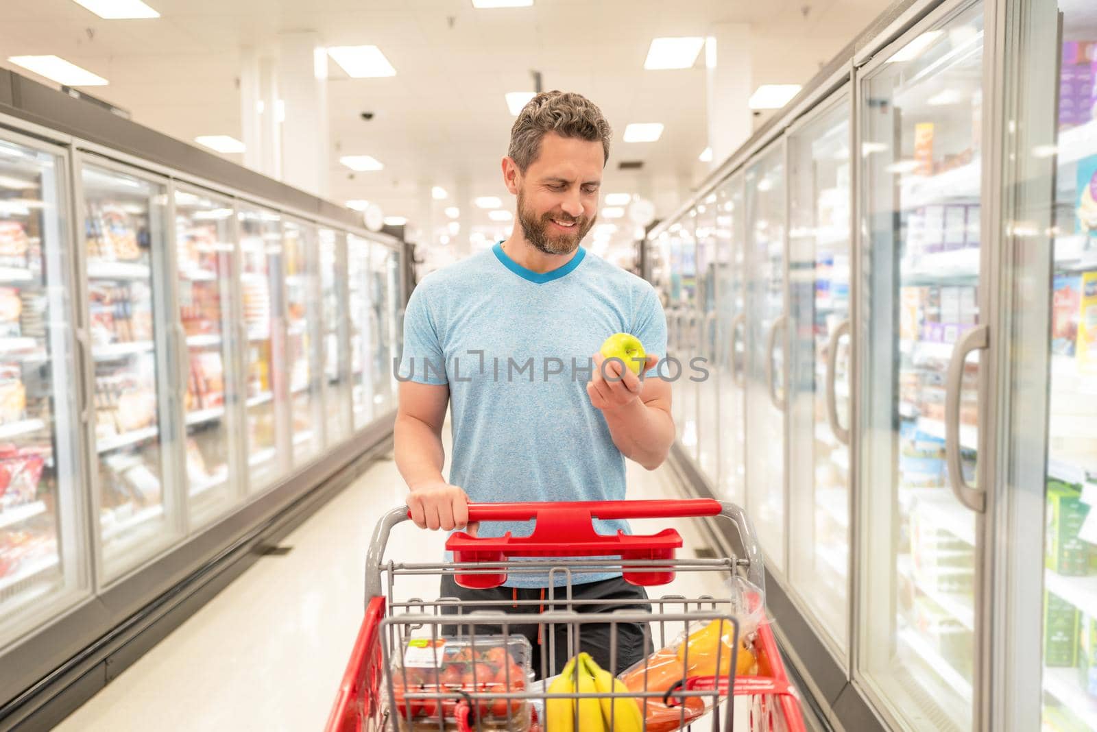 happy man with shopping cart hold apple. customer consumer with purchases. by RedFoxStudio