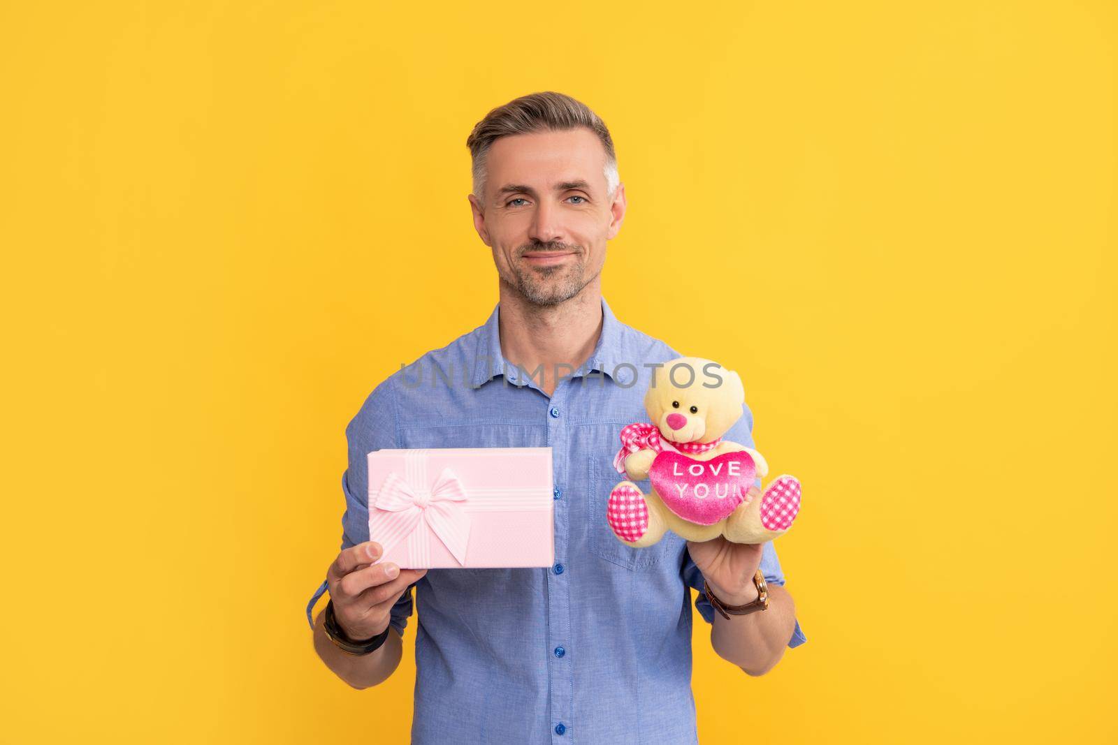 happy grizzled guy holding box and toy on yellow background, love.