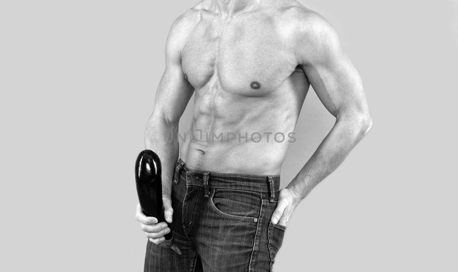 Muscular man with six pack abs torso cropped view hold firm and large eggplant at crotch level grey background, penis enlargement.