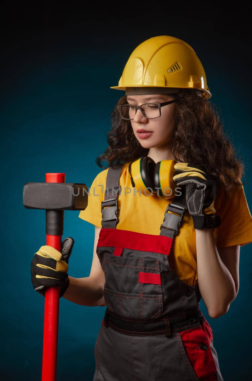 girl in the construction helmet and overalls with a sledgehammer