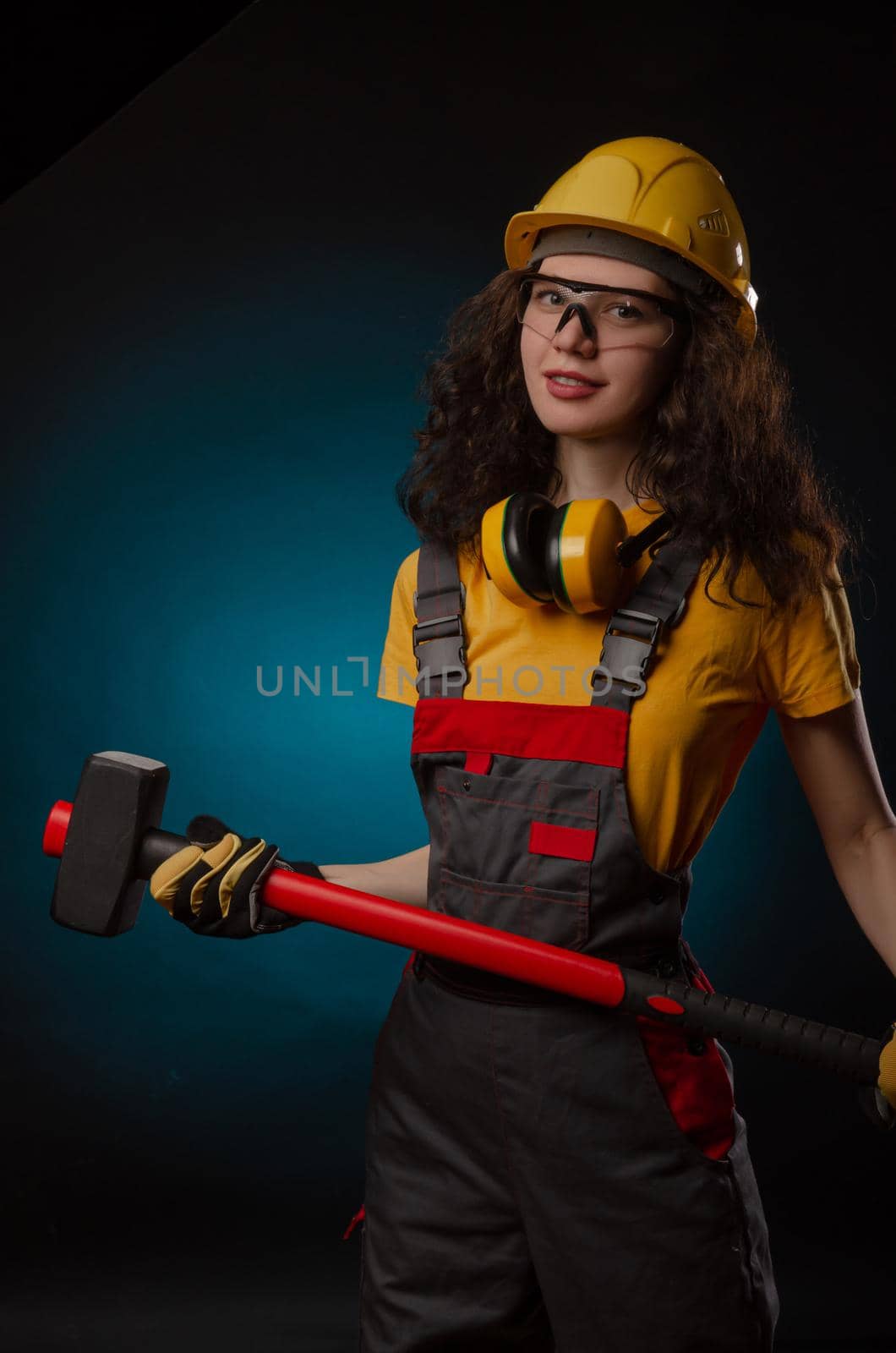 girl in the construction helmet and overalls with a sledgehammer