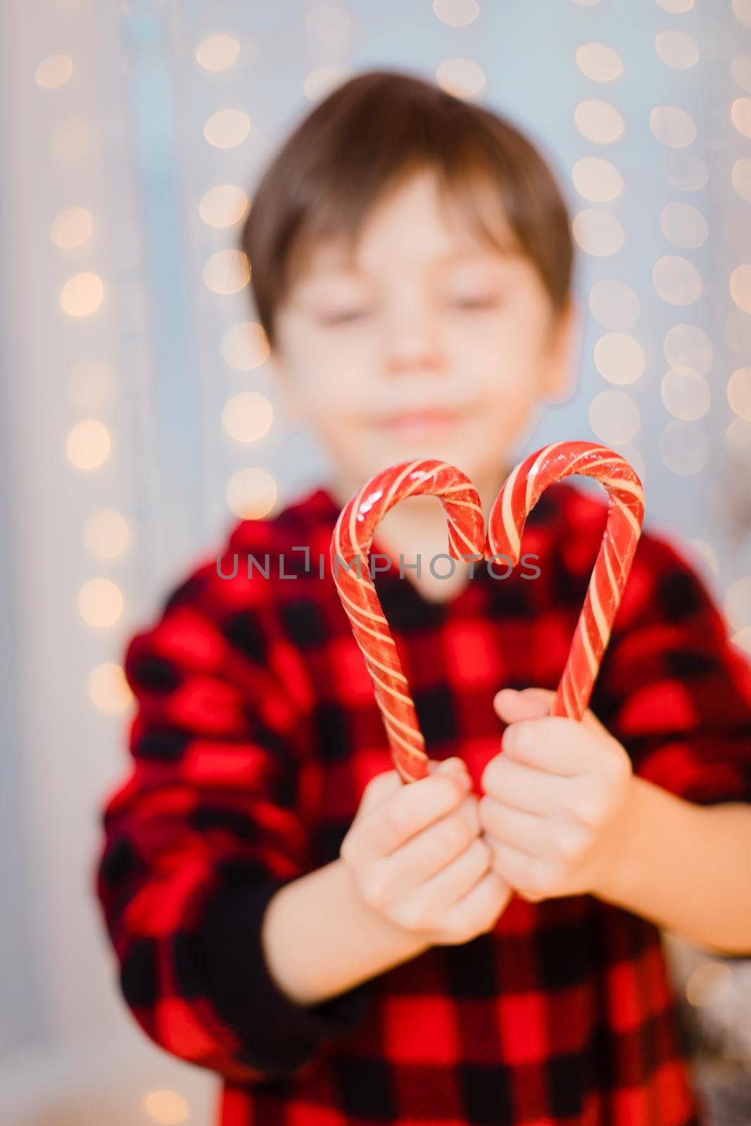 A boy in pajamas with caramel under the Christmas tree . New Year's candies are red. New Year's mood.
