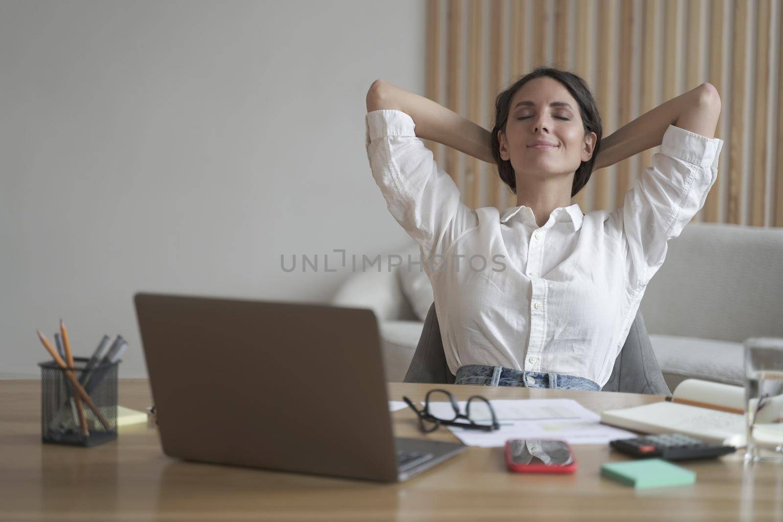 Young happy italian woman with hands behind head relaxing at workplace in home office by vkstock