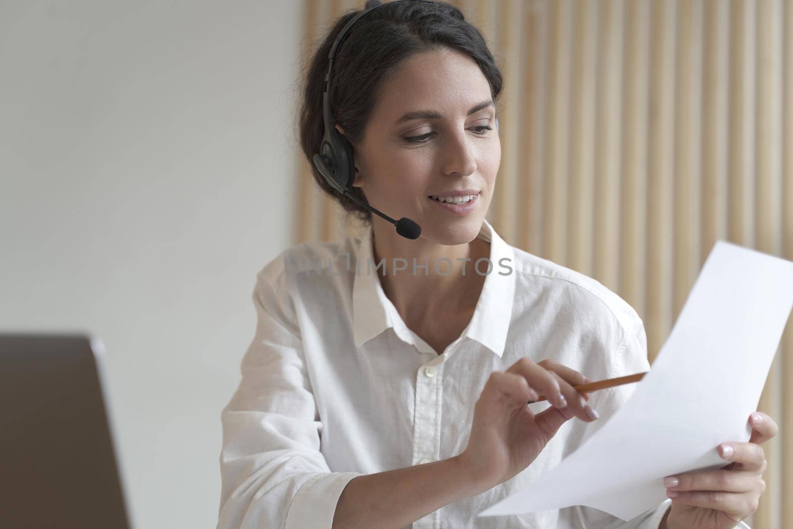 Positive Spanish businesswoman in headset sits at desk having video conference online with partners by vkstock