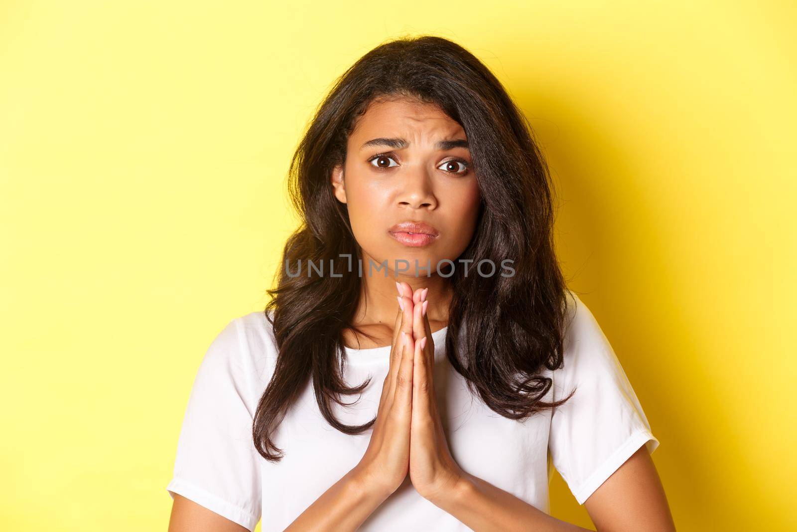 Close-up of worried african-american girl pleading, begging for help and looking gloomy, standing over yellow background.